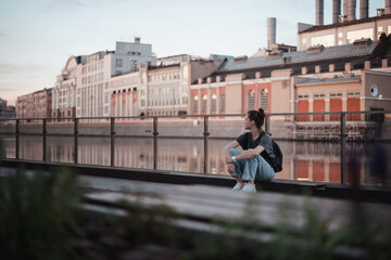 Fototapeta na wymiar Young pensive beautiful woman sitting on the embankment in the city at sunrise