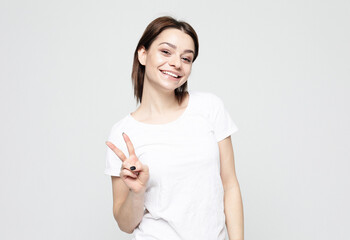 Young people, emotion and lifestyle concept: young woman with short hair wearing show victory sign over grey background