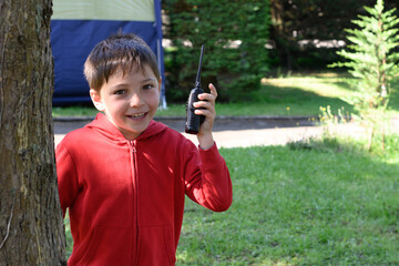 Portrait of a child looking at the camera. The boy is holding a walkie talkie in his hand and is in a camping site