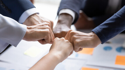 Diverse business team making group fist bump. Employees engaged in teamwork, keeping community spirit, expressing solidarity, trust, unity, friendship. Close up of multiethnic hands - obrazy, fototapety, plakaty
