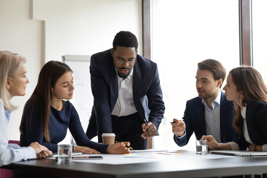 Serious African American team leader talking to employees, discussing project, reviewing sales result on corporate meeting. Business coach, teacher training group of interns, explaining documents - Powered by Adobe
