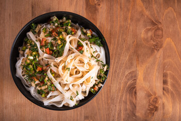 Rice noodles with hot sauce with garlic, hot pepper and spices in a black cup on a wooden table, top view, close-up, copy space for recipe