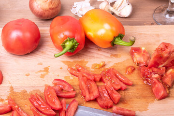 Cooking tomato, bell pepper, onion and garlic vegetable sauce for italian pasta - chopped tomatoes on a board with ingredients on the table