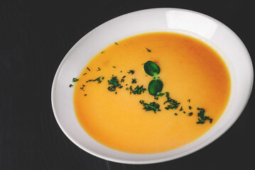 Pumpkin soup in white plate on black wooden table background