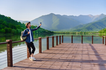 Obraz premium Hipster traveler backpacker standing alone on pier with lake and mountains view. Enjoying beautiful freedom moment life and serene quiet peaceful atmosphere in nature. Copy space
