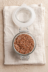 Flax seed in glass jar and napkin on beige stone background. Close-up. Flat lay.