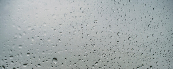 Horizontal water drops background. Wide close up on rain droplets with sharp focus on the window. Concept of moody day, nostalgia, home time and feelings.