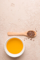 Flax seed oil in white bowl and flaxseed in wooden spoon on beige stone background. Flat lay. Copy space.