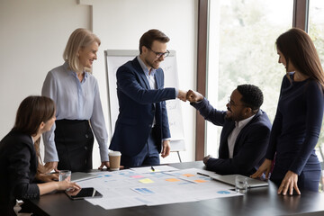 Happy excited diverse male office buddies making fist bump at workplace, expressing respect for work achievement. Corporate friends, workers, colleagues celebrating group business success