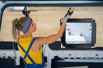 Horizontal shot of a woman, from behind, inside her DIY camper van, taking measurements of the wall.