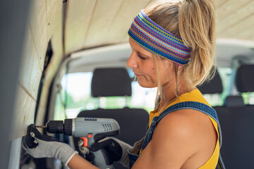 Close up of a Woman screwing in the wooden wall of her DIY camper van with a drill.
