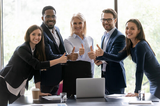 Happy diverse business team making thumbs up gesture. Group of different aged office staff, mature leader and multiethnic employees, interns and teacher showing like at camera. Corporate portrait