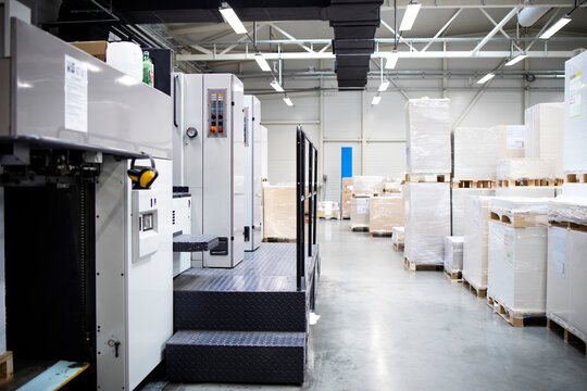 Printing shop or factory interior with modern offset paper machine and piles of sheets in background.