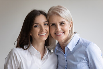 Head shot cheek to cheek portrait of happy senior 60s mother and young grownup daughter. Cute teen...
