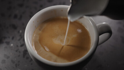 Making cappuccino, pour steamed milk into white cup with espresso