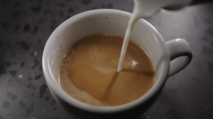 Making cappuccino, pour steamed milk into white cup with espresso