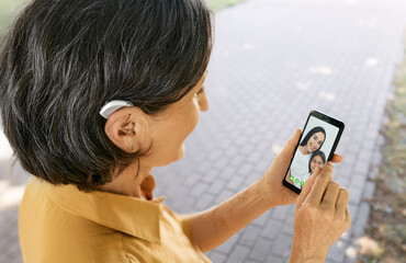 Senior woman with a hearing aid behind the ear communicates with her daughter and granddaughter via...