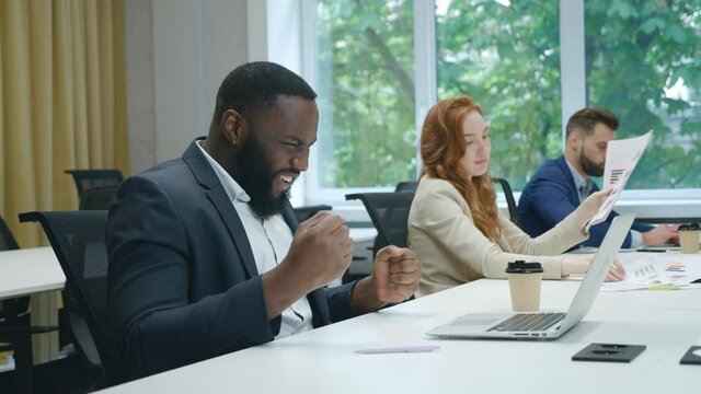 Overjoyed african businessman in suit looking at laptop screen, excited by unbelievable good news at office. Surprised man celebrating good results in front of laptop in office, showing yes sign