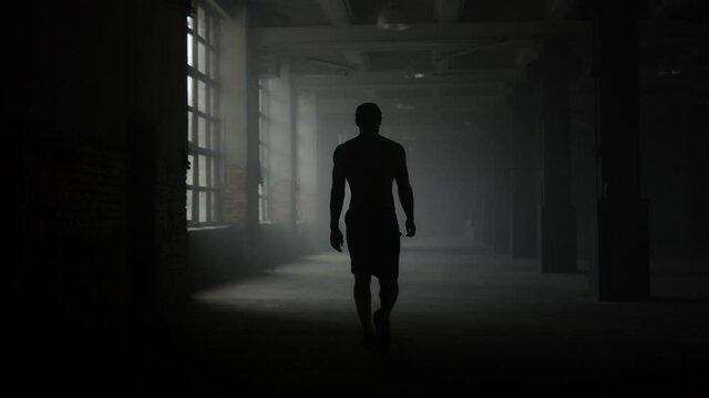 Man silhouette walking in dark corridor. Athlete taking break after workout
