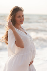Fototapeta na wymiar Beautiful calm pregnant woman wear white dress posing over sea at background closeup. Healthy lifestyle. Motherhood. Maternity. Haapiness.