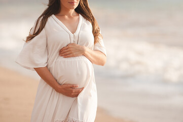 Smiling pregnant woman wear white dress hol tummy walk at beach over sea nature background...
