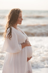 Beautiful calm pregnant woman wear white dress posing over sea at background closeup. Healthy lifestyle. Motherhood. Maternity.