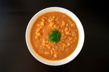 Arabic cuisine - plain peeled fava beans in a white bowl on a dark brown background. Top view. Foul Mudammas