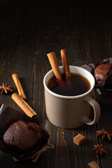 Cream ceramic cup with black tea and brown sugar, cinnamon and star anise on a dark wooden background, delicious chocolate muffins for tea