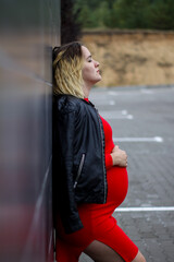 young pregnant girl in a red dress in the parking lot. pregnancy is a joy. big pregnant belly. new life.