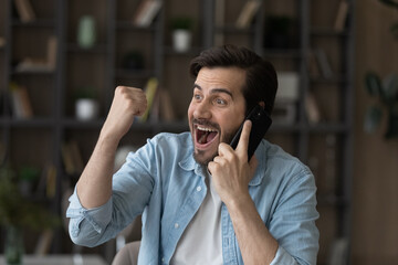 Candid emotional young businessman entrepreneur manager listening amazing news, holding cellphone...