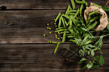 green young peas in pods, freshly picked on old brown boards, top view, empty space for text