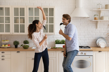 Funny cooking together. Playful young husband wife prepare food at modern domestic kitchen enjoy singing songs listen to music. Happy millennial married couple relax having fun while making breakfast
