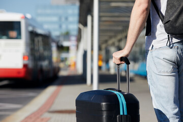Passenger waiting at bus station in front of airport terminal. Selective focus on hand holding suitcace. © Chalabala