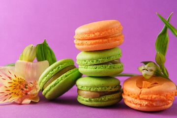 sweets, green and beige macaroon cookies, flowers on a purple background,