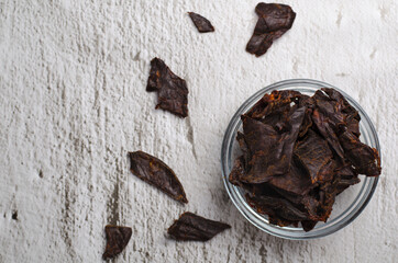 Jerky meat on a concrete background. Dried beef. Glassware. Copy space. Close-up. Flat lay.