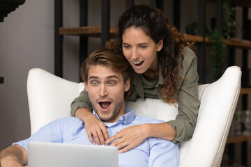 Unbelievable. Shocked millennial couple in love look on laptop screen with big eyes getting money...