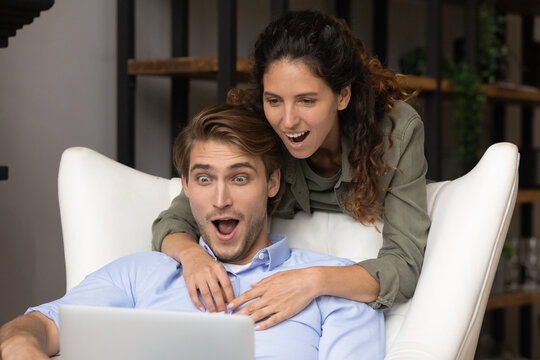 Unbelievable. Shocked millennial couple in love look on laptop screen with big eyes getting money prize at online betting. Excited young spouses overwhelmed by great discount cheap tickets at website