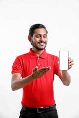 Portrait of a excited happy young delivery man in red t shirt and showing smartphone over white background.