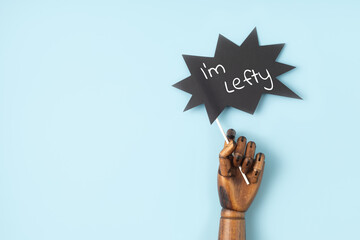 Wooden mannequin hand with sign i am lefty over blue background. International left handers day...