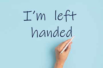 Text I am left handed and left hand with pen over blue background. International left handers day concept