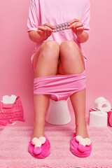 Vertical shot of unrecognizable woman suffers from strng stomachache poses in bathroom on toilet...