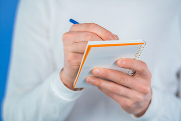 Man hands making notes in planner, caucasian guy holding pen. He writes future plans and to-do list in notebook for week or month. Keeping personal diary on blue studio background.