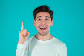 Young thinking pondering man having idea moment pointing finger up on blue studio background. Smiling happy guy showing eureka gesture, he found answer.