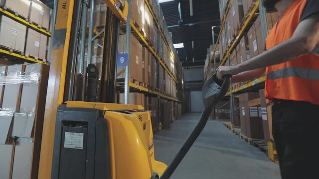 Worker with forklift in the warehouse. The worker walks through the warehouse. A worker in a warehouse carries a electric hydraulic forklift