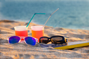 Refreshments, sun glasses and a book for a relaxing day on the beach. Preparing for a quit, sunny day near the sea.