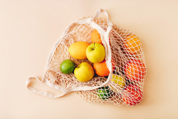 Mesh shopping bag with fresh fruits on light colored background. Zero waste, plastic free concept.