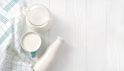 Milk in mug and jug of milk and napkin on white wooden table. Top view flat lay. Bottle of milk on...