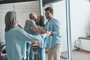Obraz premium Smiling senior parents meeting young couple inside the house