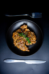 Steak on the plate and black background sprinkled with salt and pepper.

