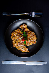 Steak on the plate and black background sprinkled with salt and pepper.
